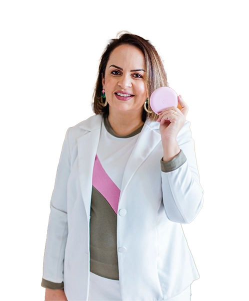 foto da Priscila Pagioro sorrindo, de pé, com uma blusa branca com rosa e marrom sob um blazer branco e uma mini-saia branca, segurando uma caixa de invisalign